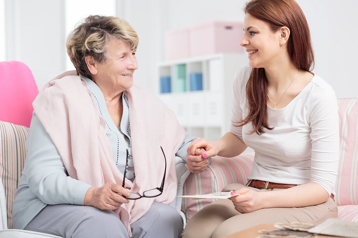 Jasmine Estates of Edmond | dementia care resources | Senior woman and caregiver sitting on couch smiling
